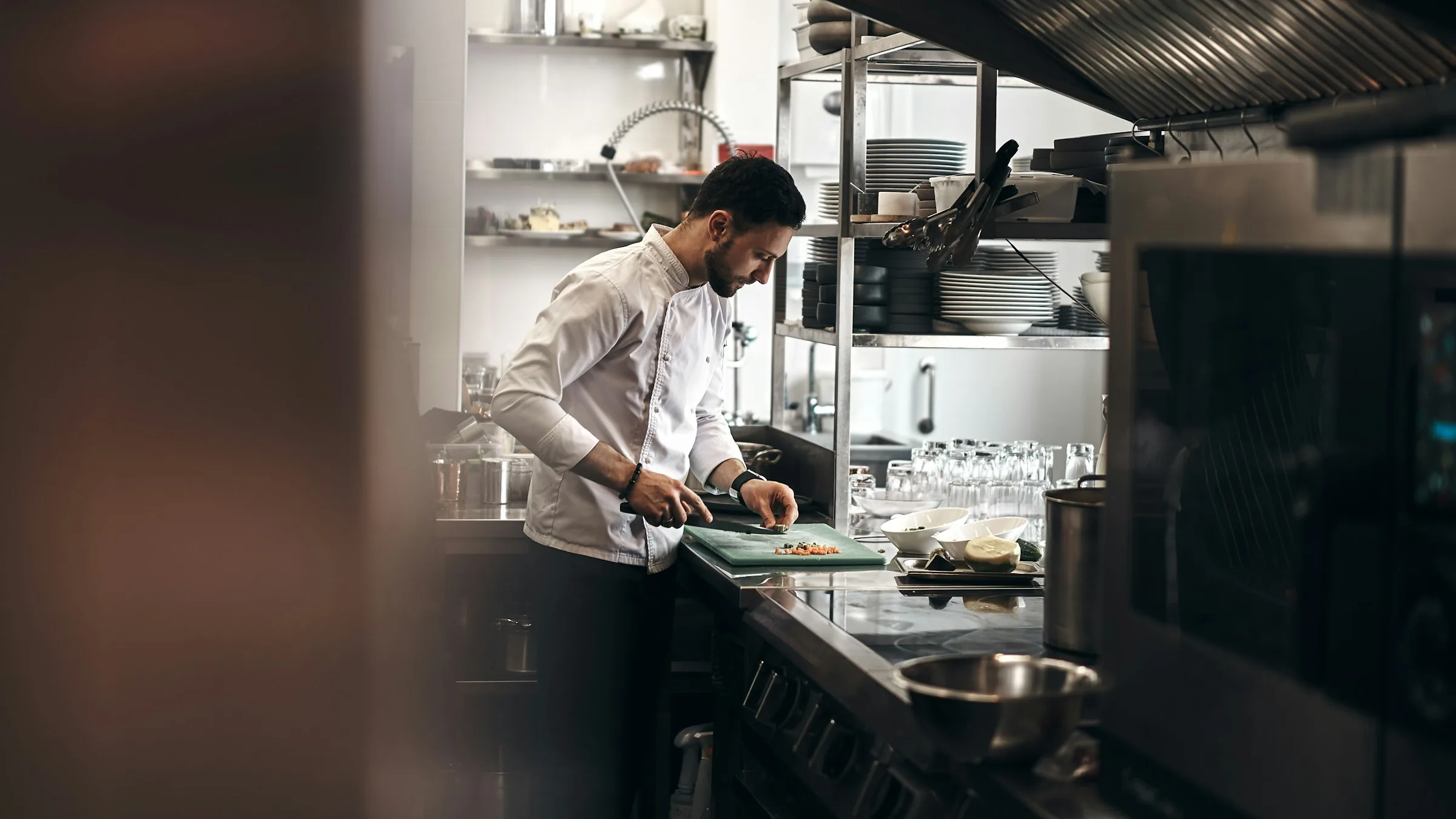 A head chef preparing a dish at the steel counter of a bright restaurant kitchen