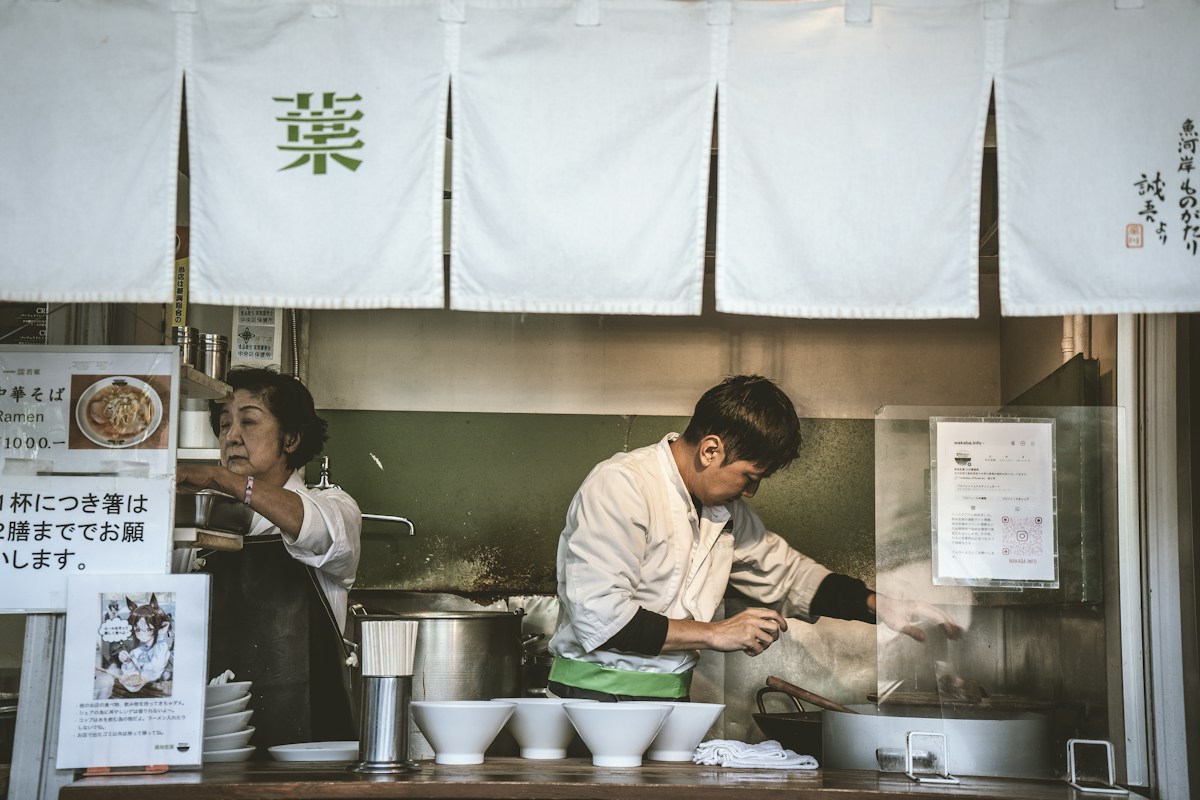 Two cooks working the pots behind white noren curtains