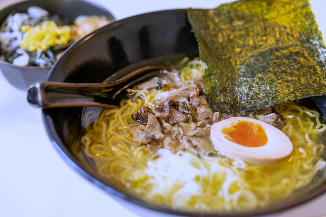 A bowl of tonkotsu at an angle with nori, a soft egg and thin noodles