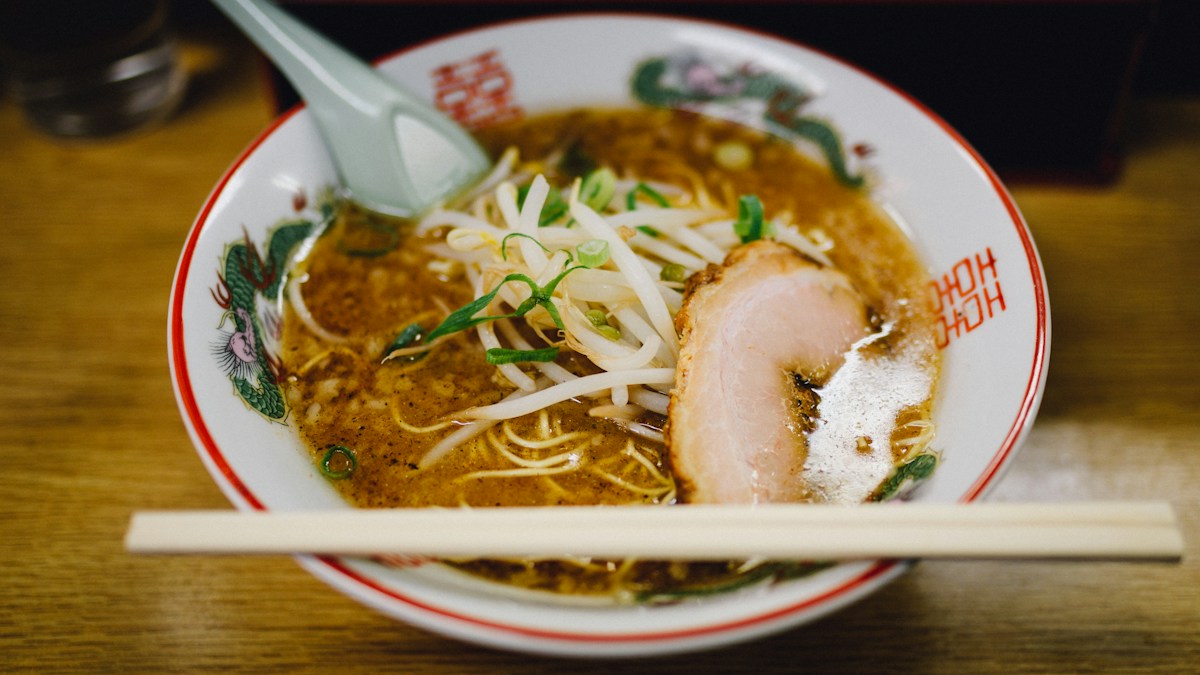 A bowl of shoyu ramen with chashu, bean sprouts and scallion, chopsticks across the rim