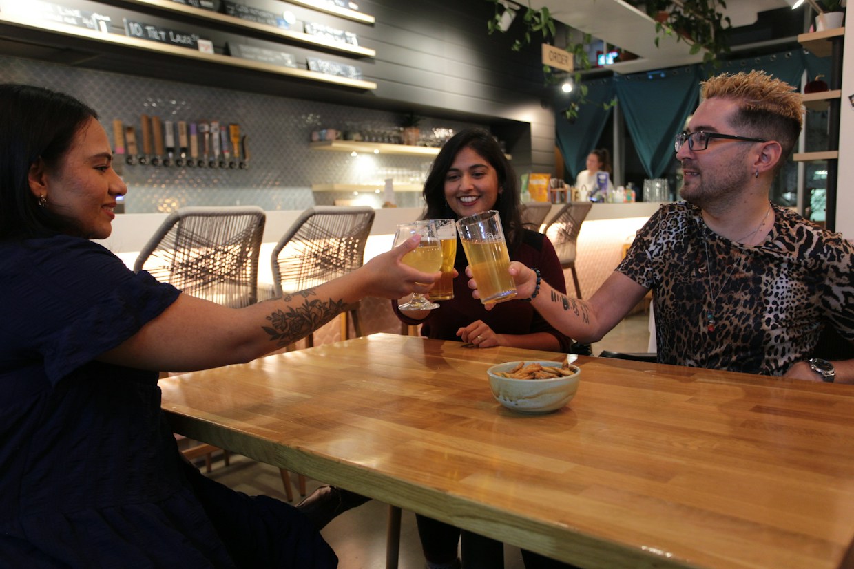Friends raise their glasses across a wooden table in a warm bar
