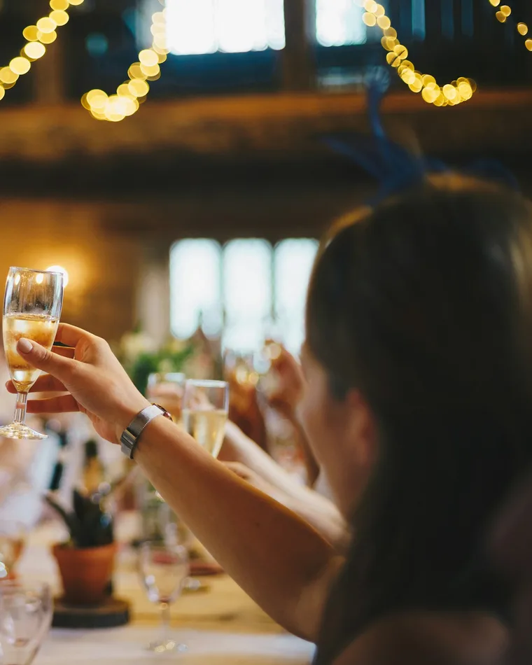 A guest raises a glass of sparkling wine under string lights