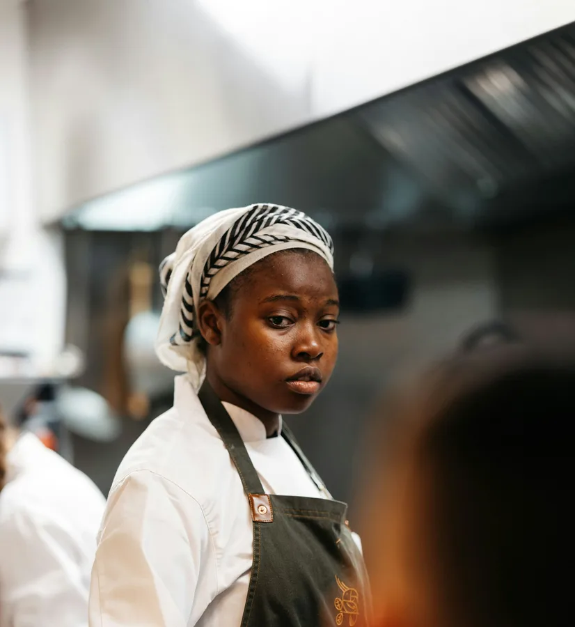 Amara Okafor in chef's whites and a headwrap at the pass