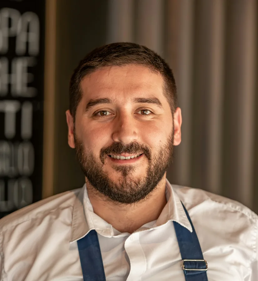 Emre Kaya in a blue apron, smiling in his restaurant