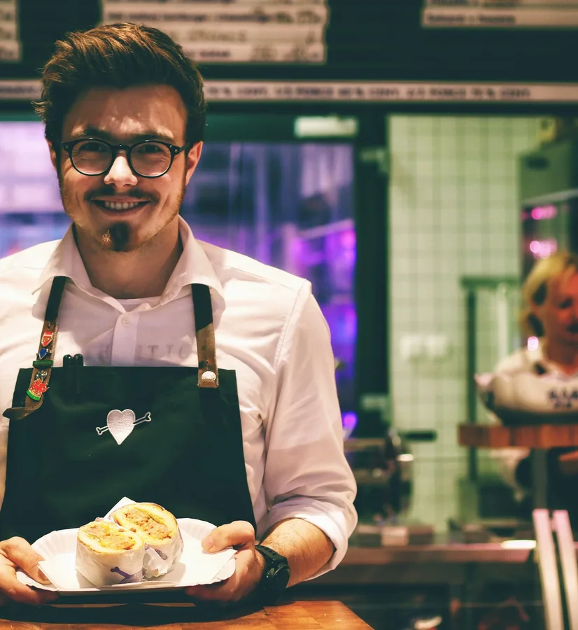 Tomás Ortega in a green apron carries a plate across his market stall