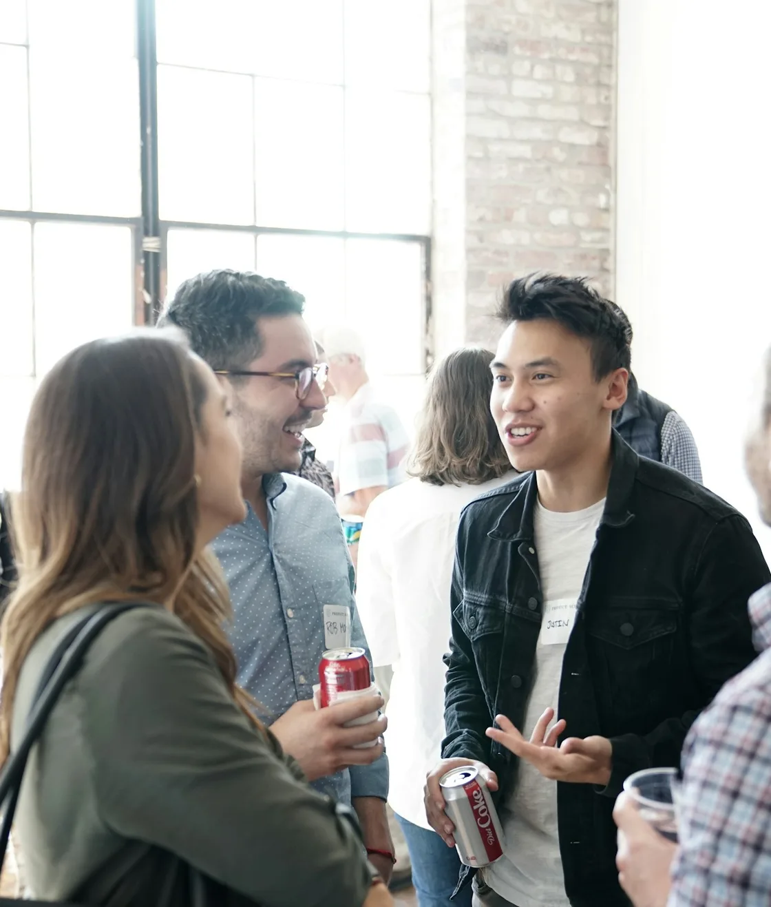 Guests talk over drinks by tall windows and a brick wall