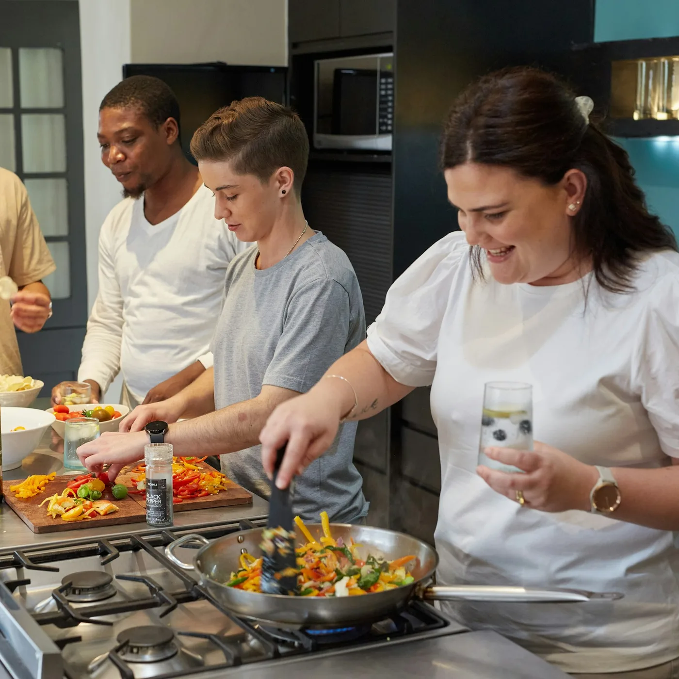 Four owners cook peppers and onions together at a steel workshop counter
