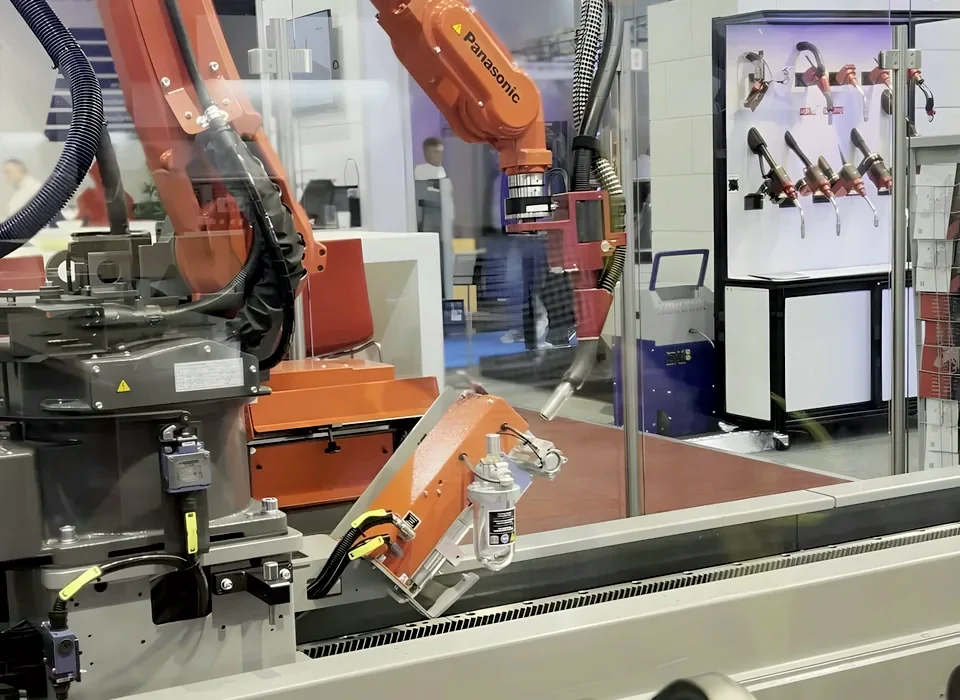 Orange welding robot with its torch over a fixture in a glass-guarded cell