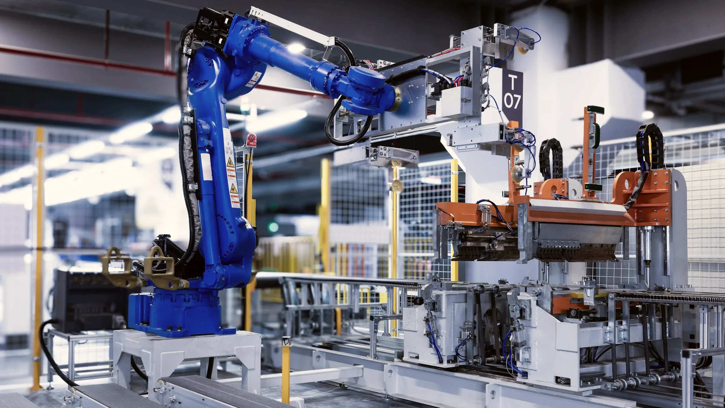 Blue industrial robot working inside a fenced machining cell on a bright plant floor