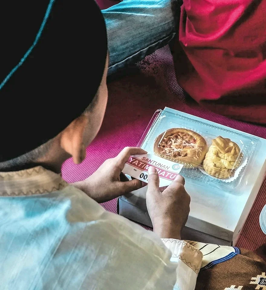 A boy holds an iftar box of fresh bread and pastries on his lap