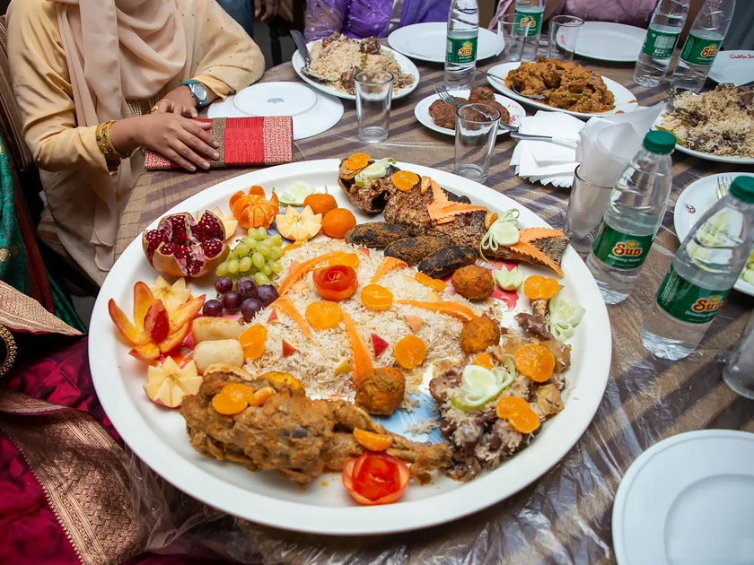 A shared iftar platter of rice, lamb, dates and fruit in the middle of a community table