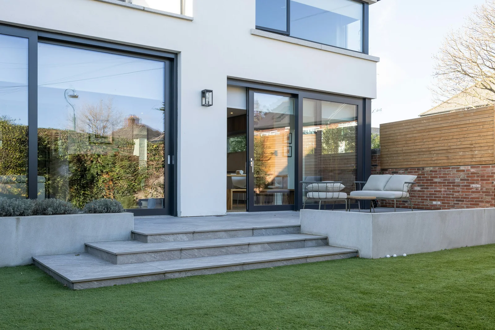 A white rendered rear extension with sliding glass doors onto stone steps and a lawn