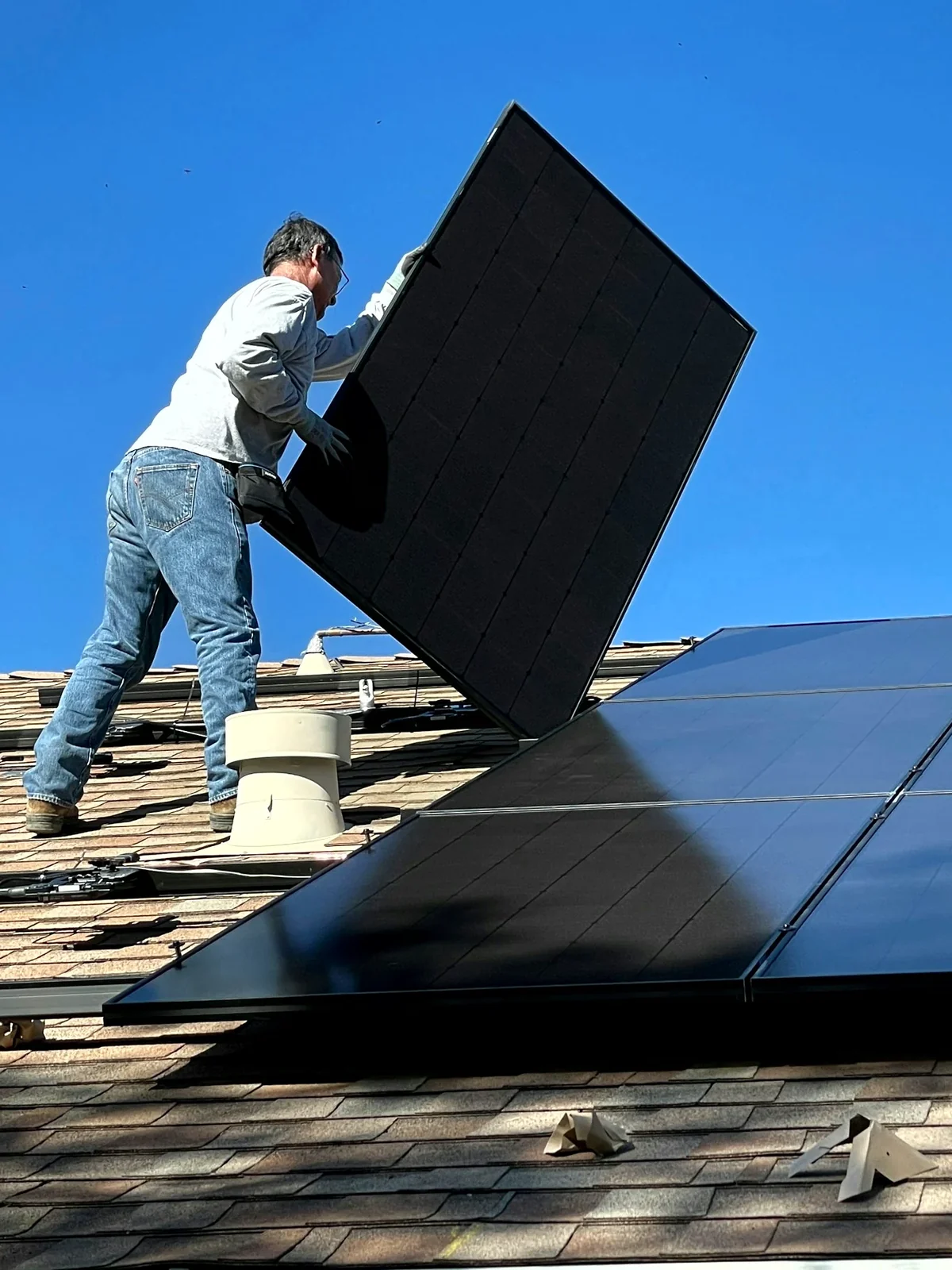 Two installers in hard hats fitting a solar panel onto a tile roof under hard Arizona sun