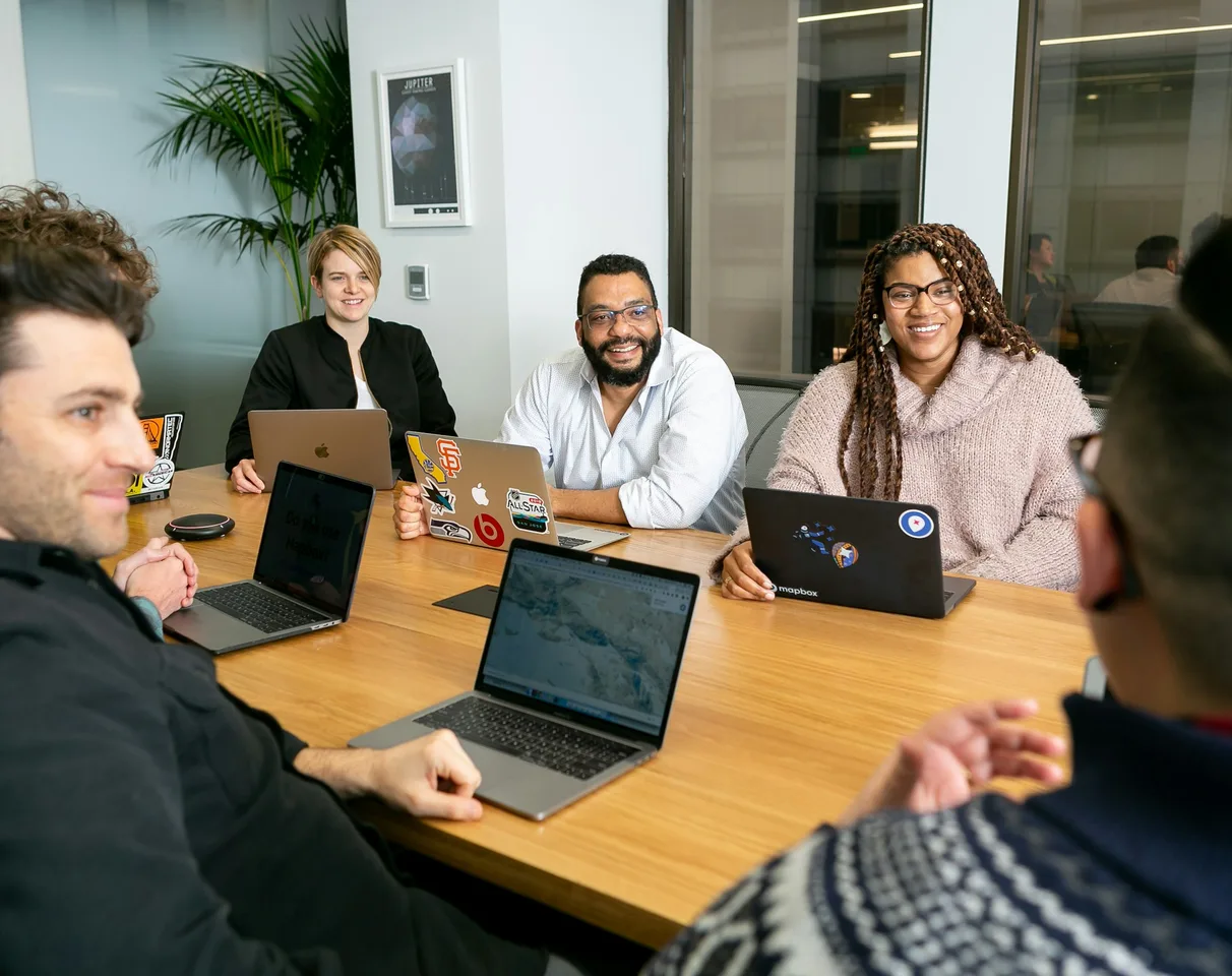 An agency team laughing around a meeting table with laptops in a bright office