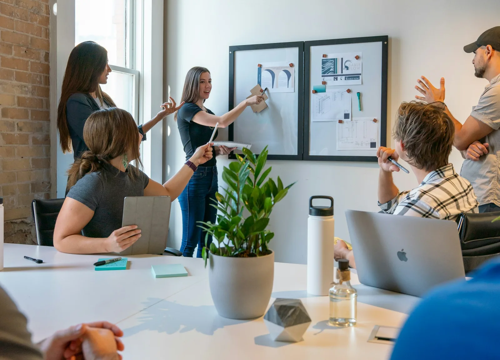 A creative studio team pinning work to a board in a bright brick-walled room