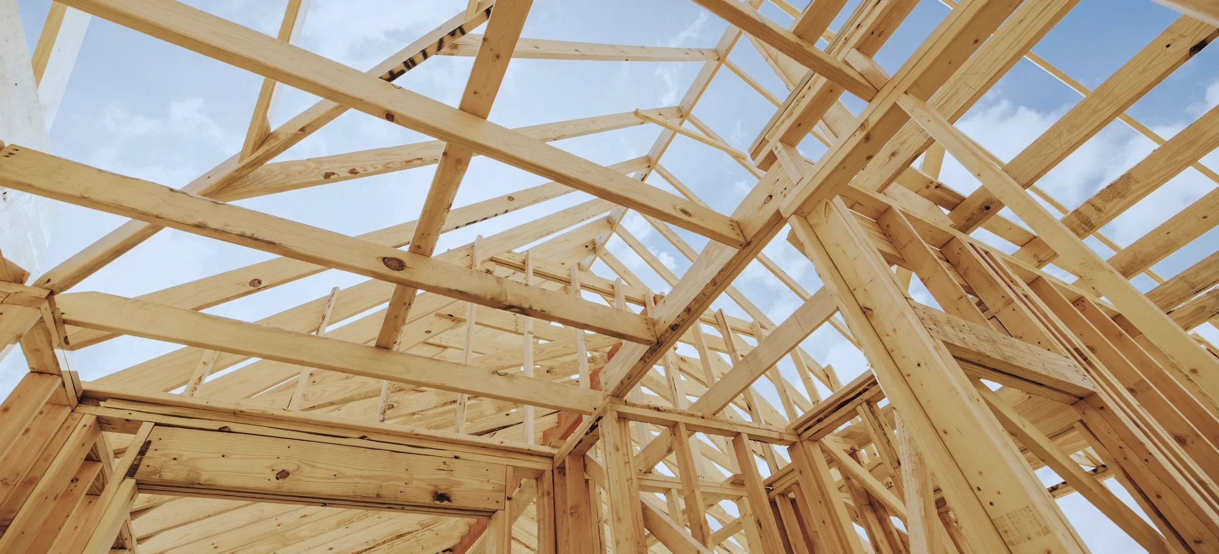 Pale timber frame of a house under construction against a clear blue sky