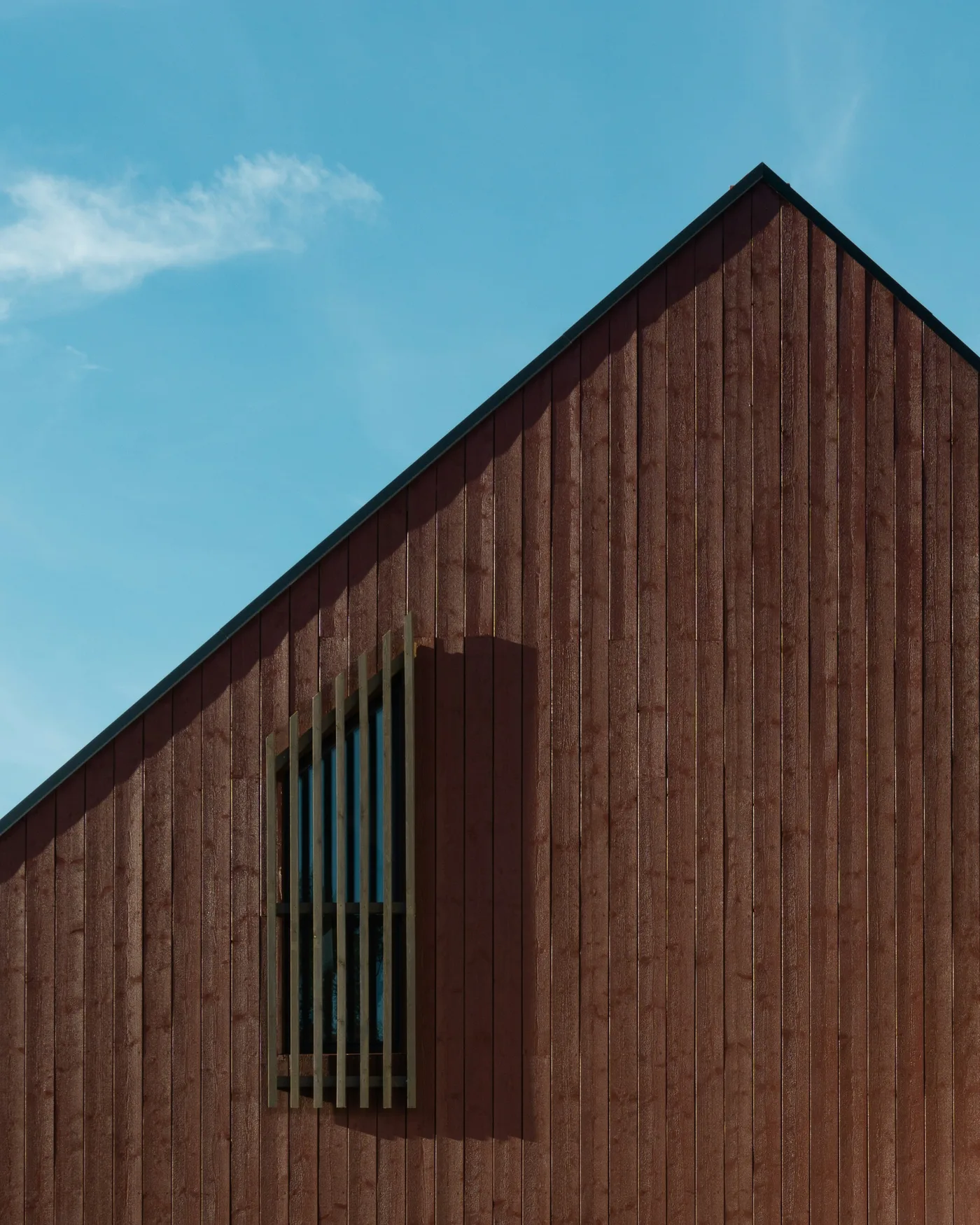 Dark timber gable of a house with a tall narrow window, against a clear blue sky