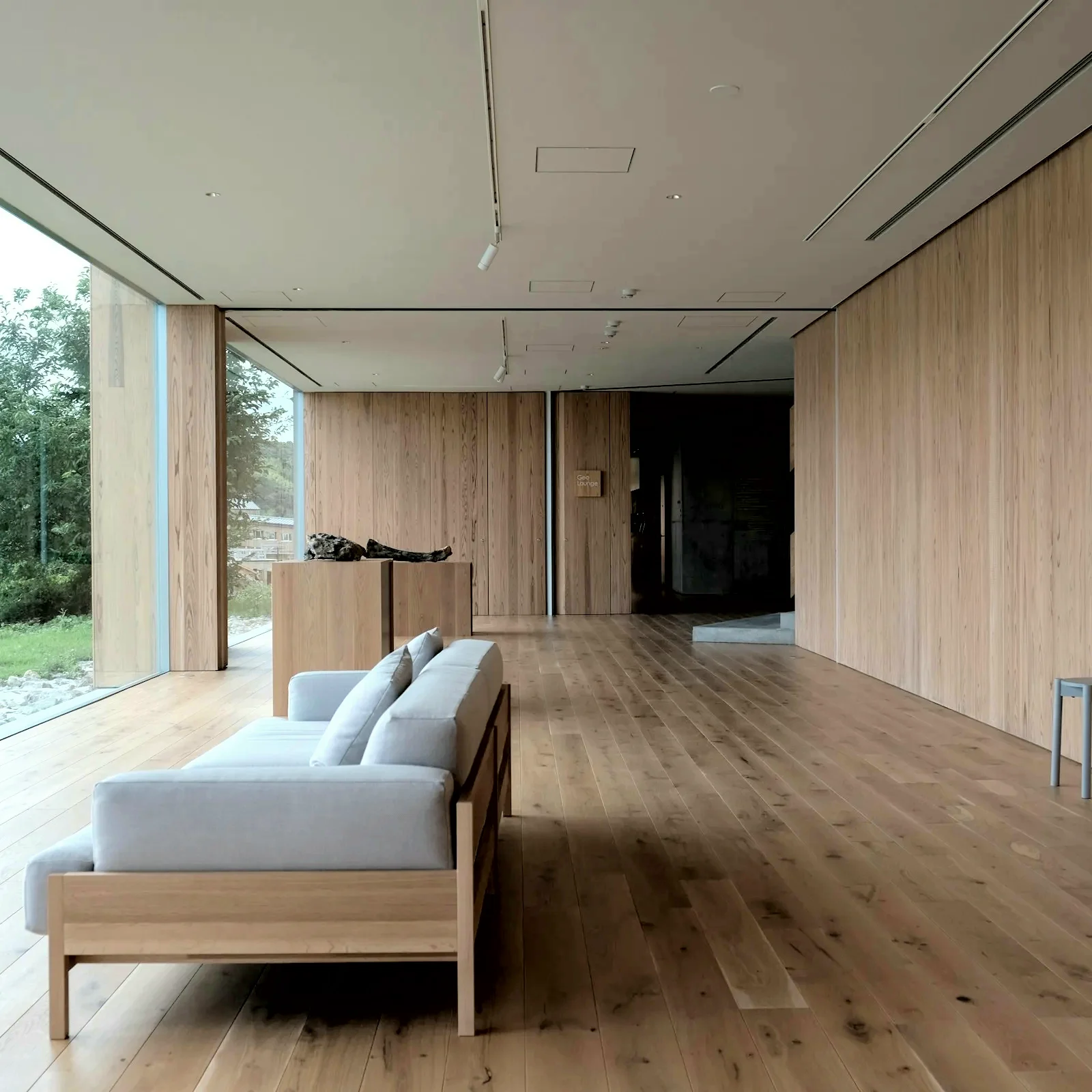 Timber living room with a pale sofa, oak floor and a full-height window onto trees