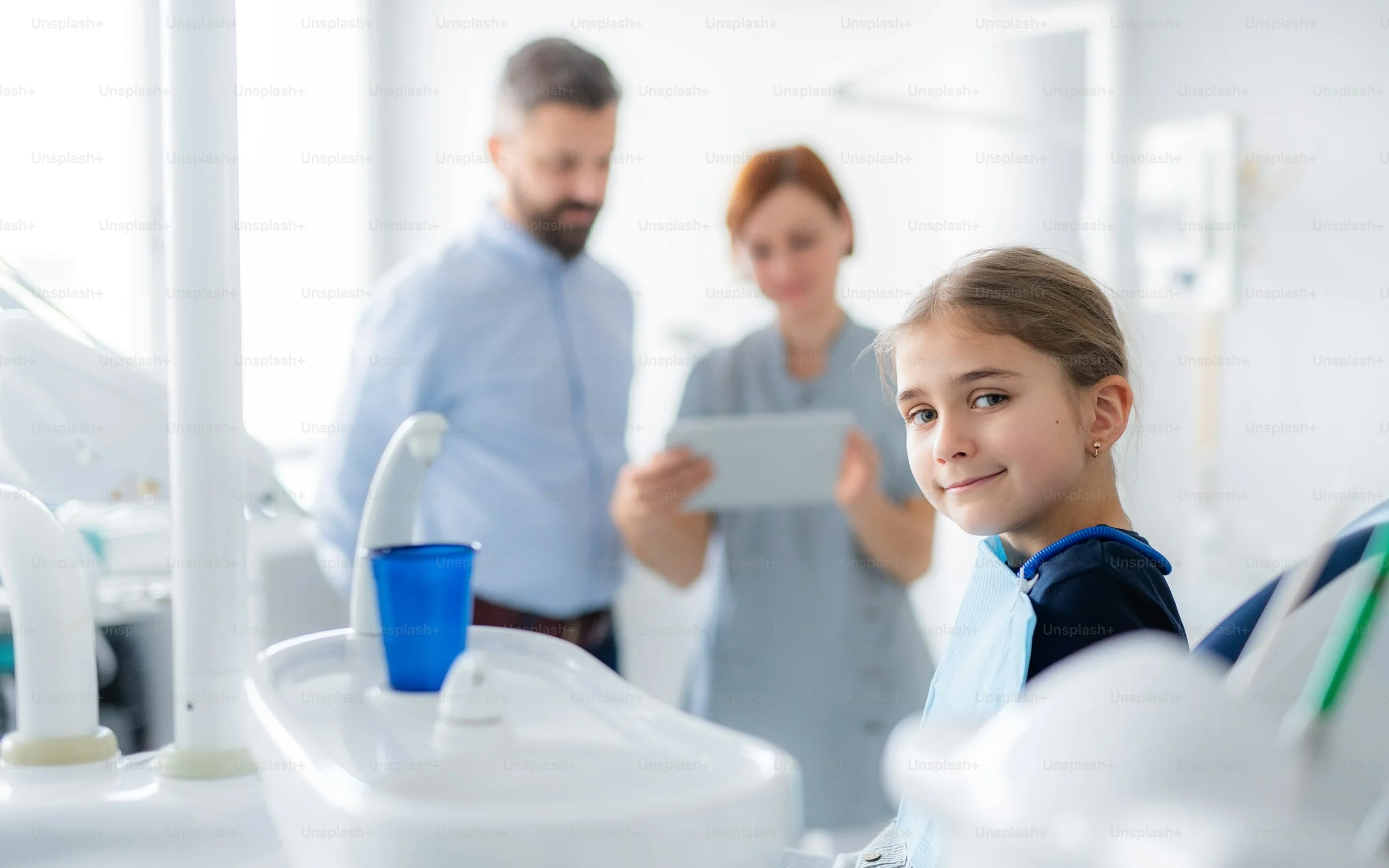 A girl in the dental chair smiles while her dad and the hygienist look at her x-ray on a tablet
