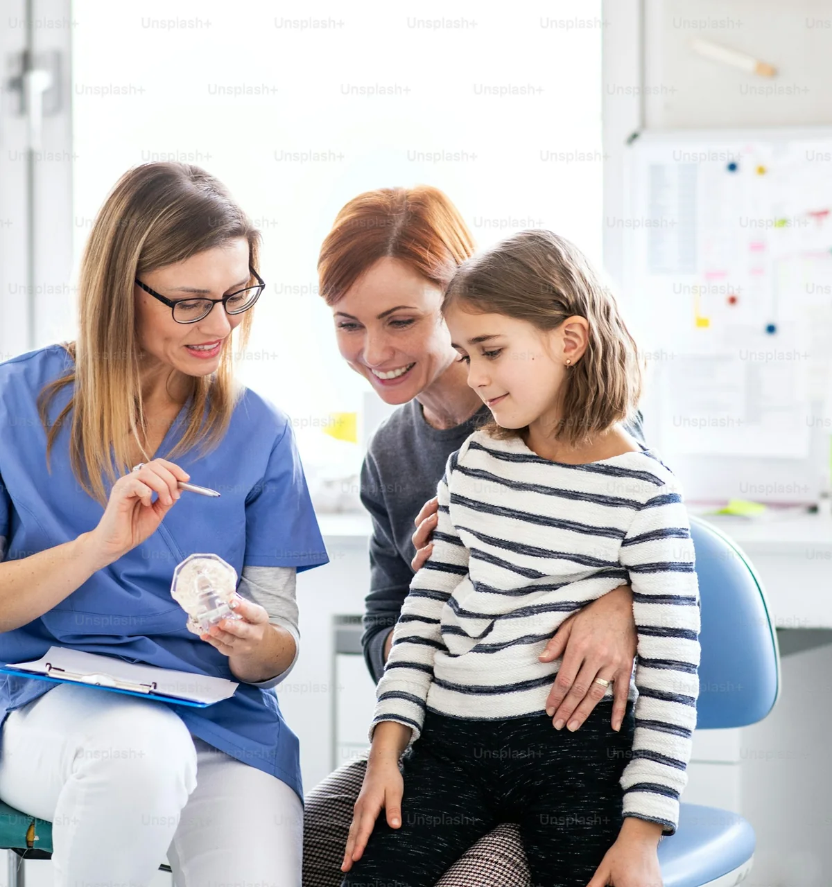A mom holds her daughter on her lap while the dentist talks them through a checkup