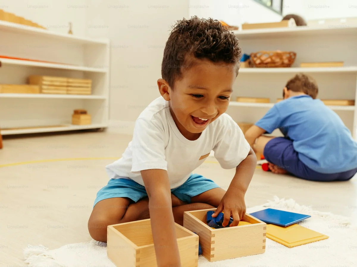 A smiling boy lifts blue blocks out of a wooden box