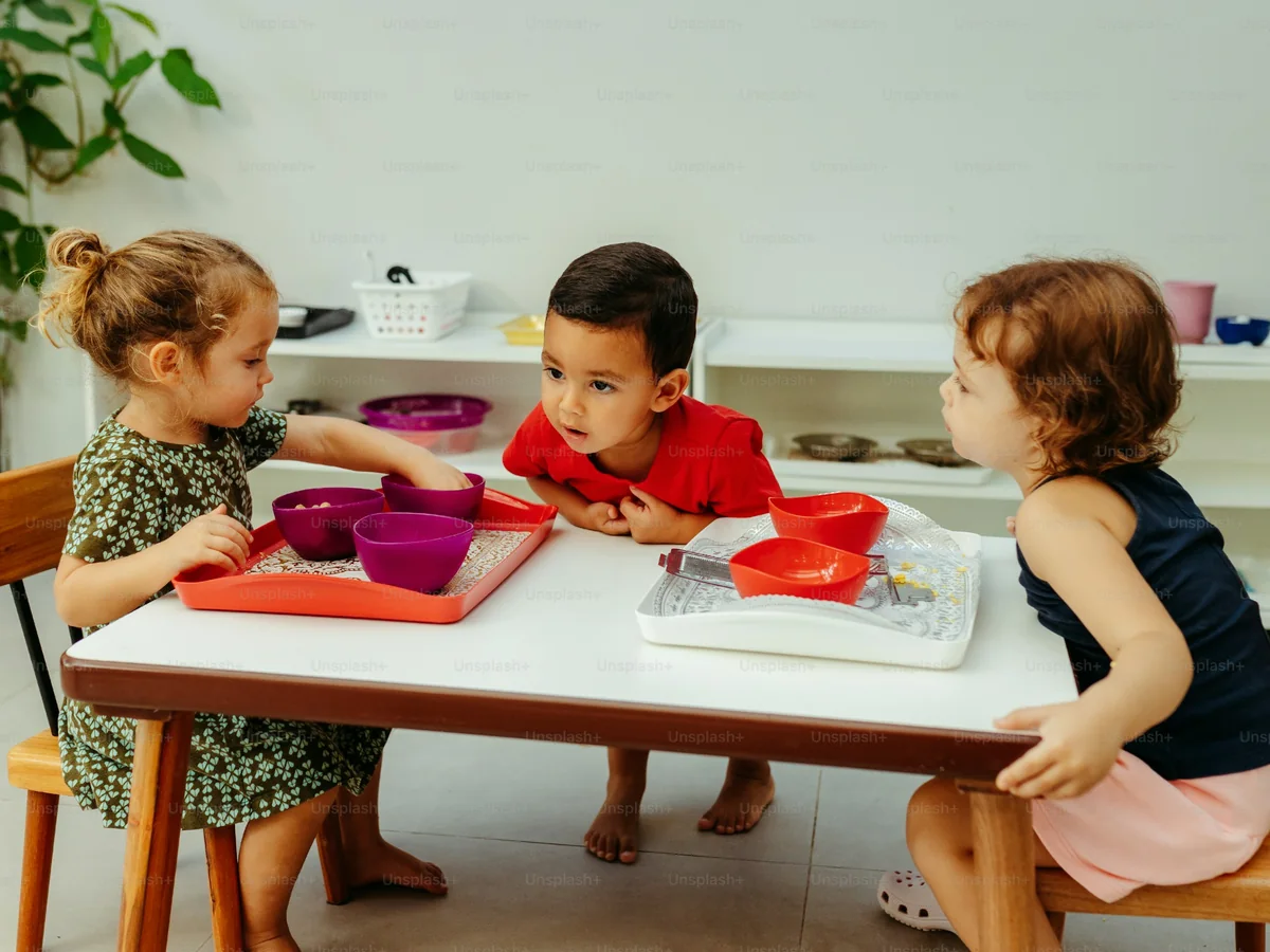 Three toddlers serve themselves fruit from bowls at a low white table