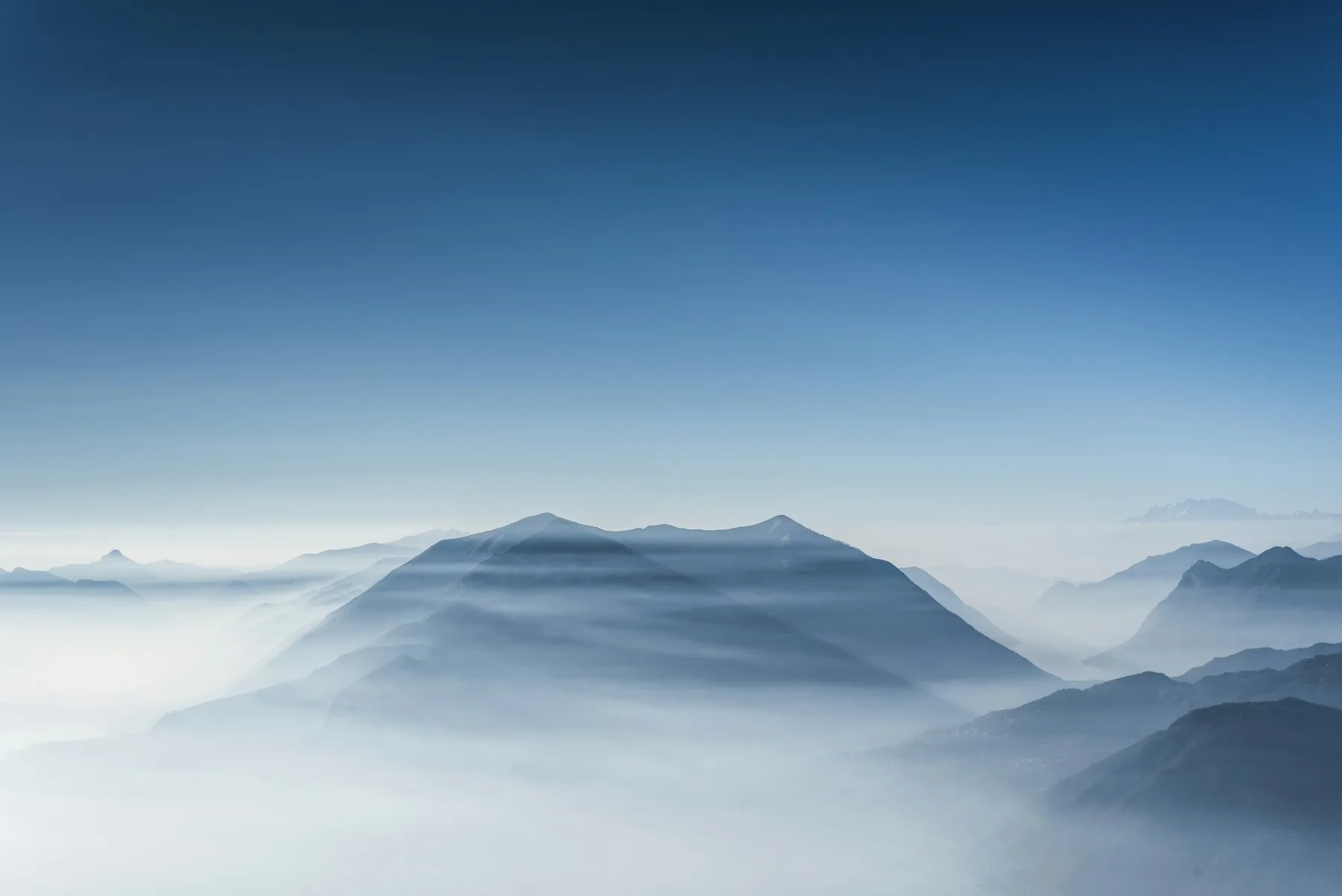 A mountain rising out of a blue sea of fog under a clear sky