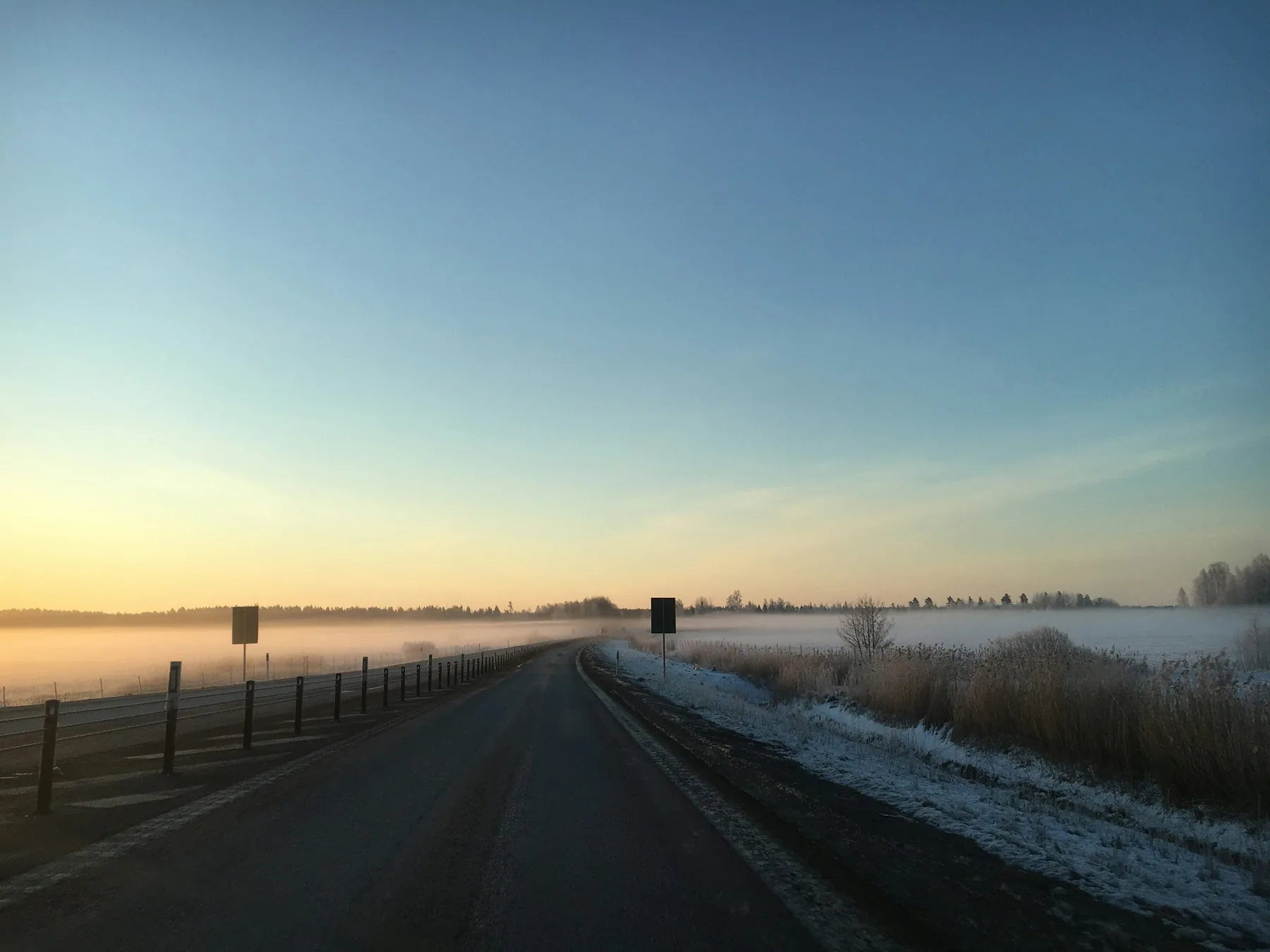 A straight country road through frosted fields at sunrise, a fence along one side