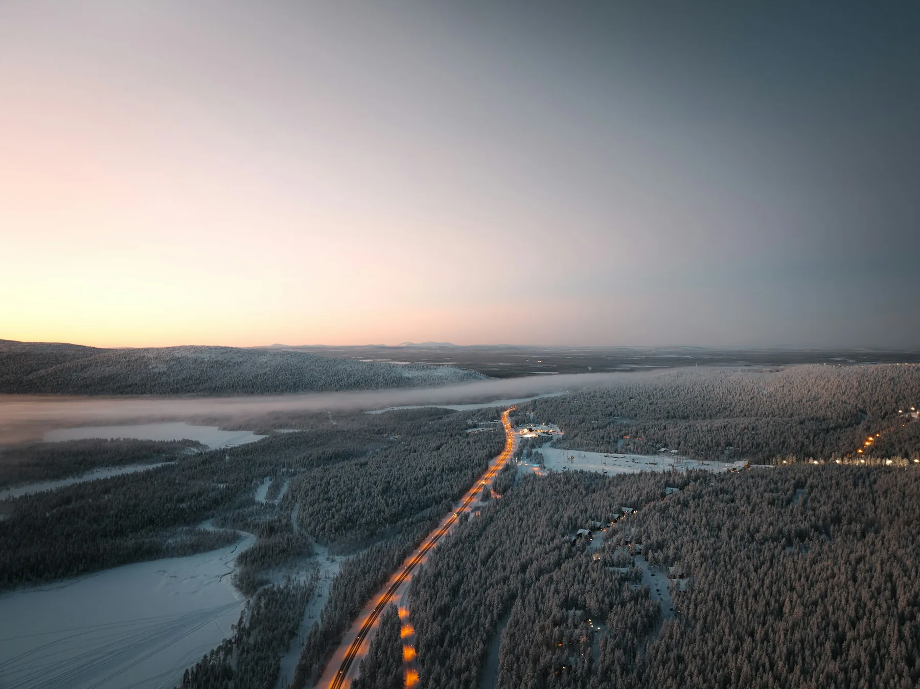 Aerial view of a road lit by headlights cutting through frosted forest before dawn