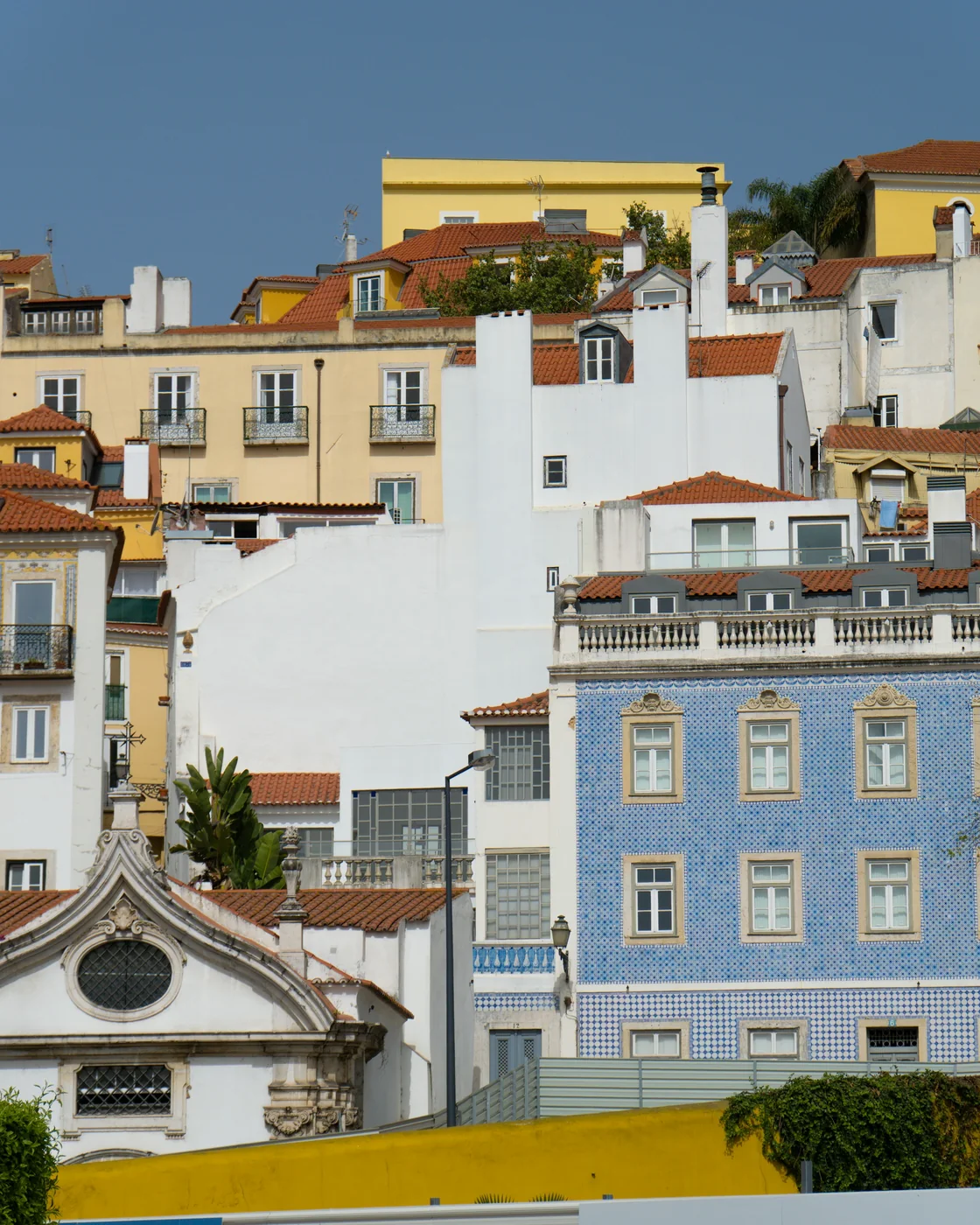 Alfama's stacked façades: a blue azulejo house, white walls and terracotta roofs in afternoon sun