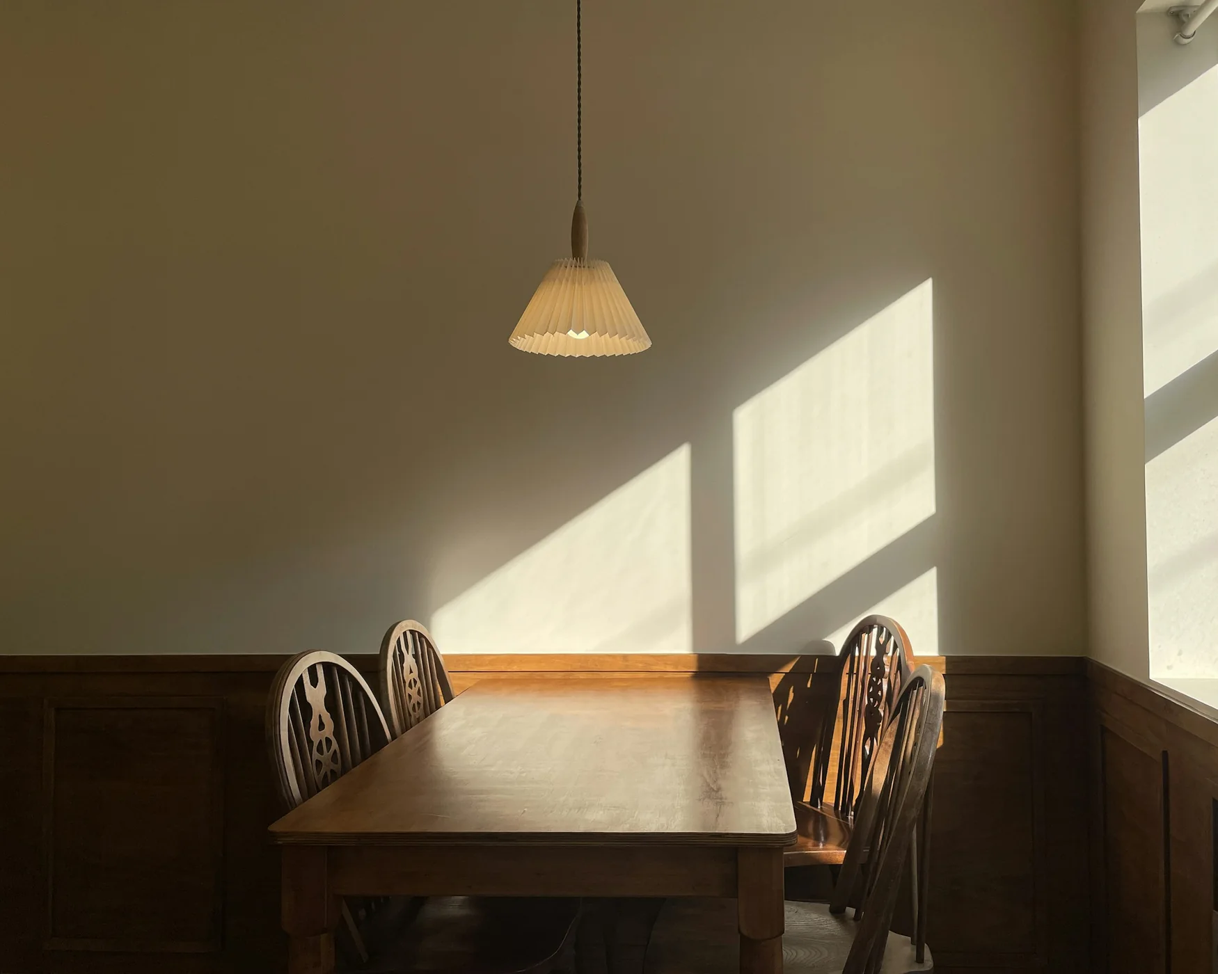 The breakfast corner at Casa Lumen: morning sun across a plaster wall, a wooden table and a paper pendant
