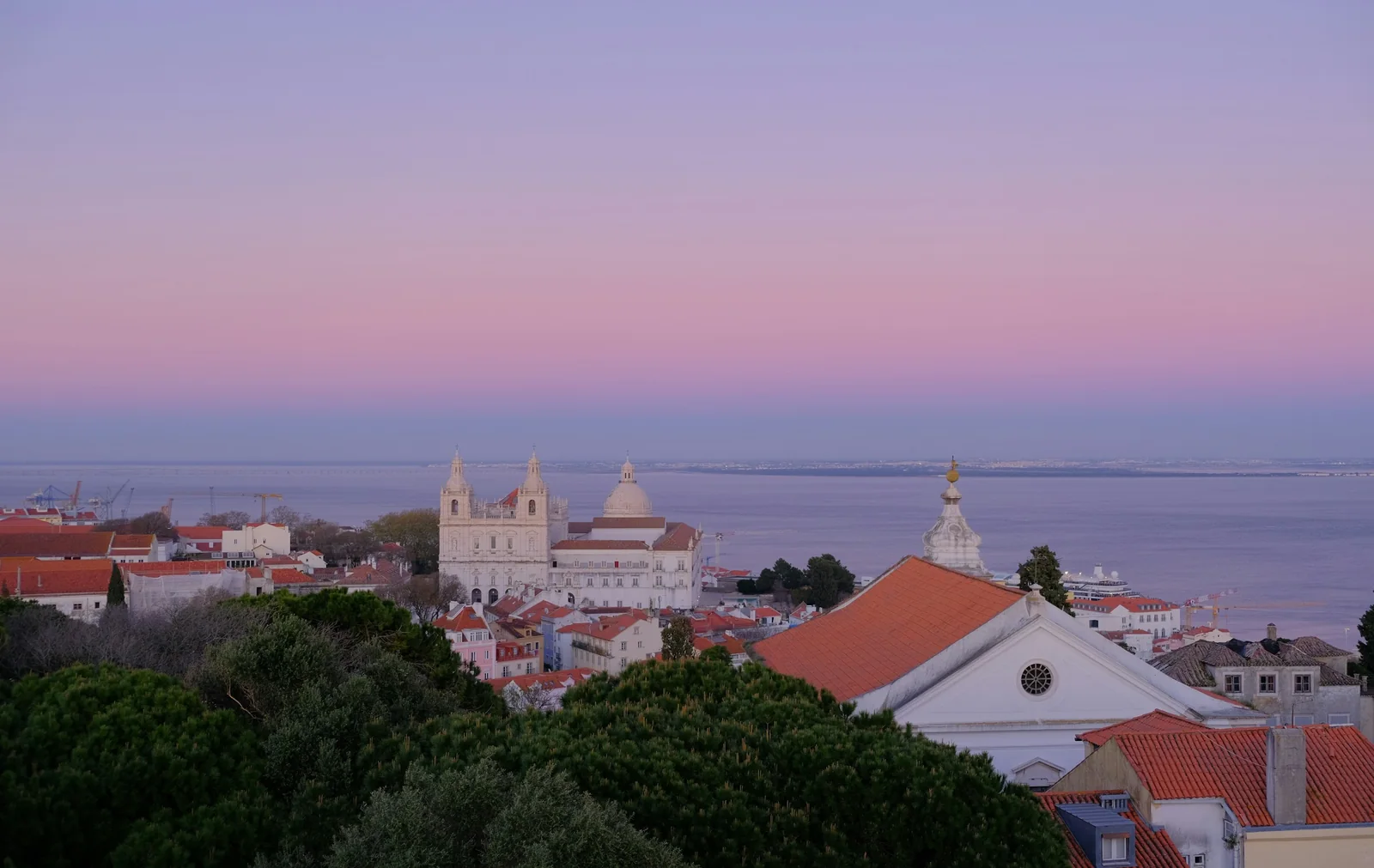 São Vicente and the Tejo from the roof of Casa Lumen at dusk, the sky pink over terracotta roofs
