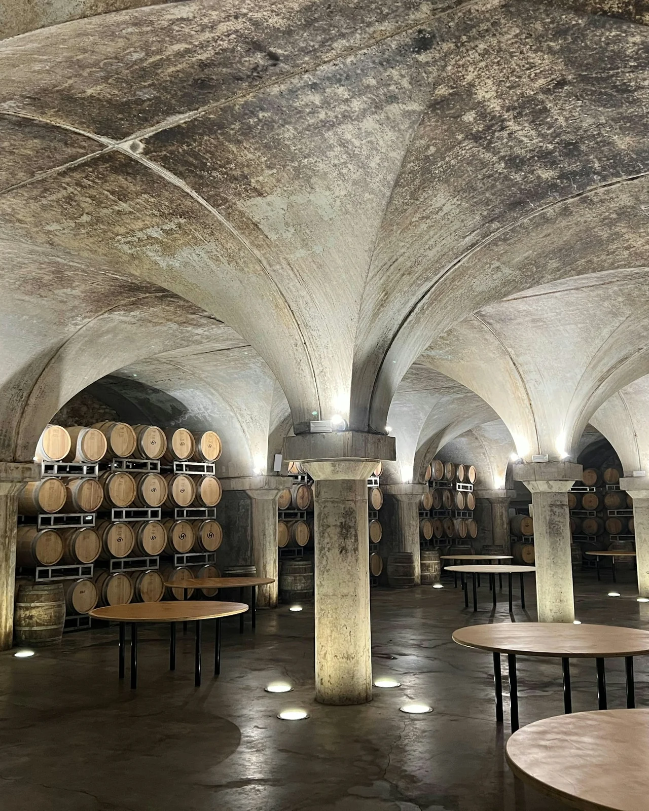 Oak barrels under an old stone vault, tasting tables set out between the pillars