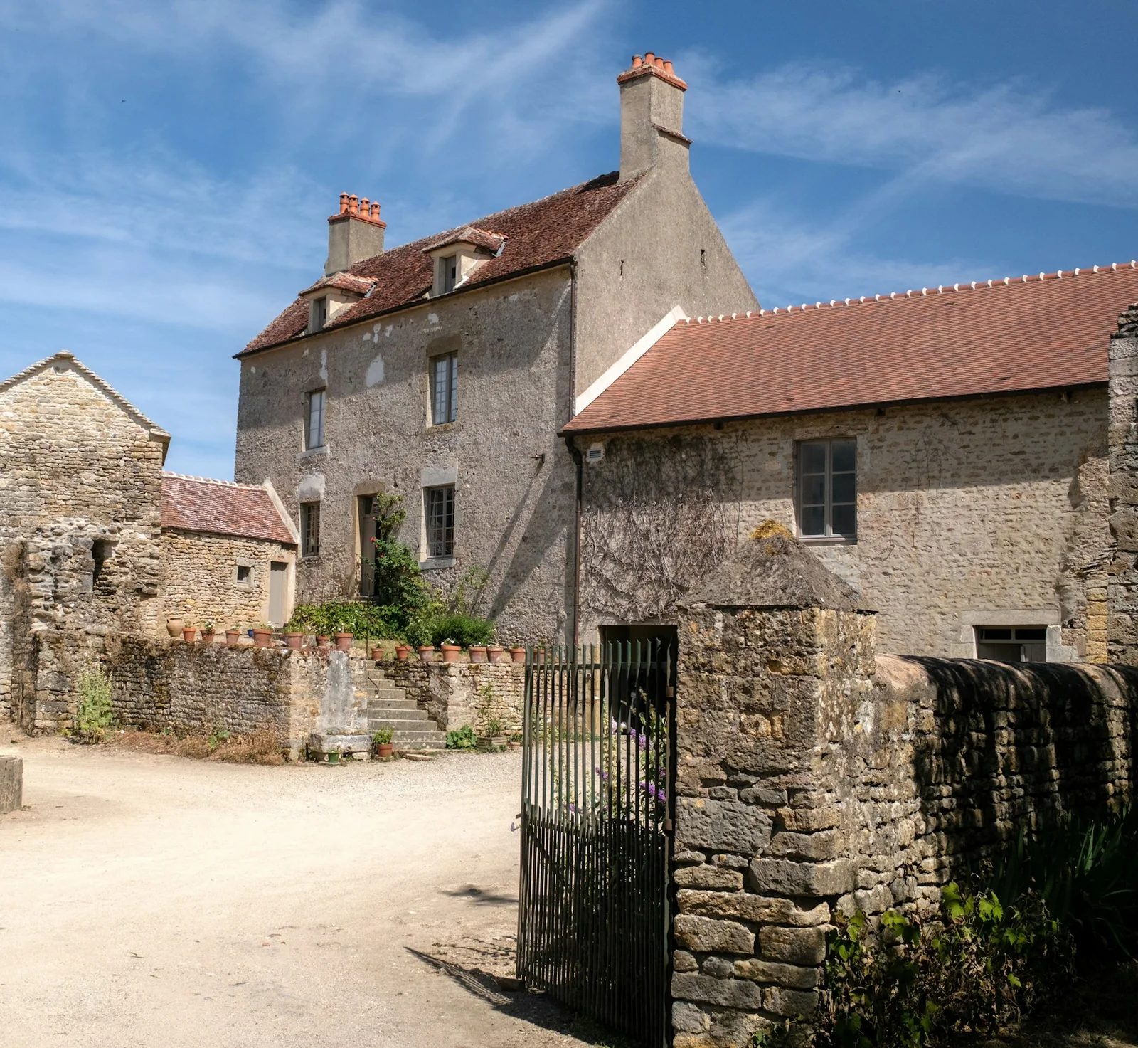 Stone farmhouse behind its courtyard wall and iron gate under a blue sky