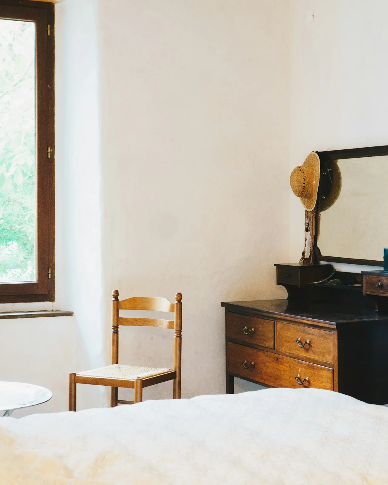Guest room in the old farmhouse: lime-washed walls, a wooden window, a rush chair and an antique dresser