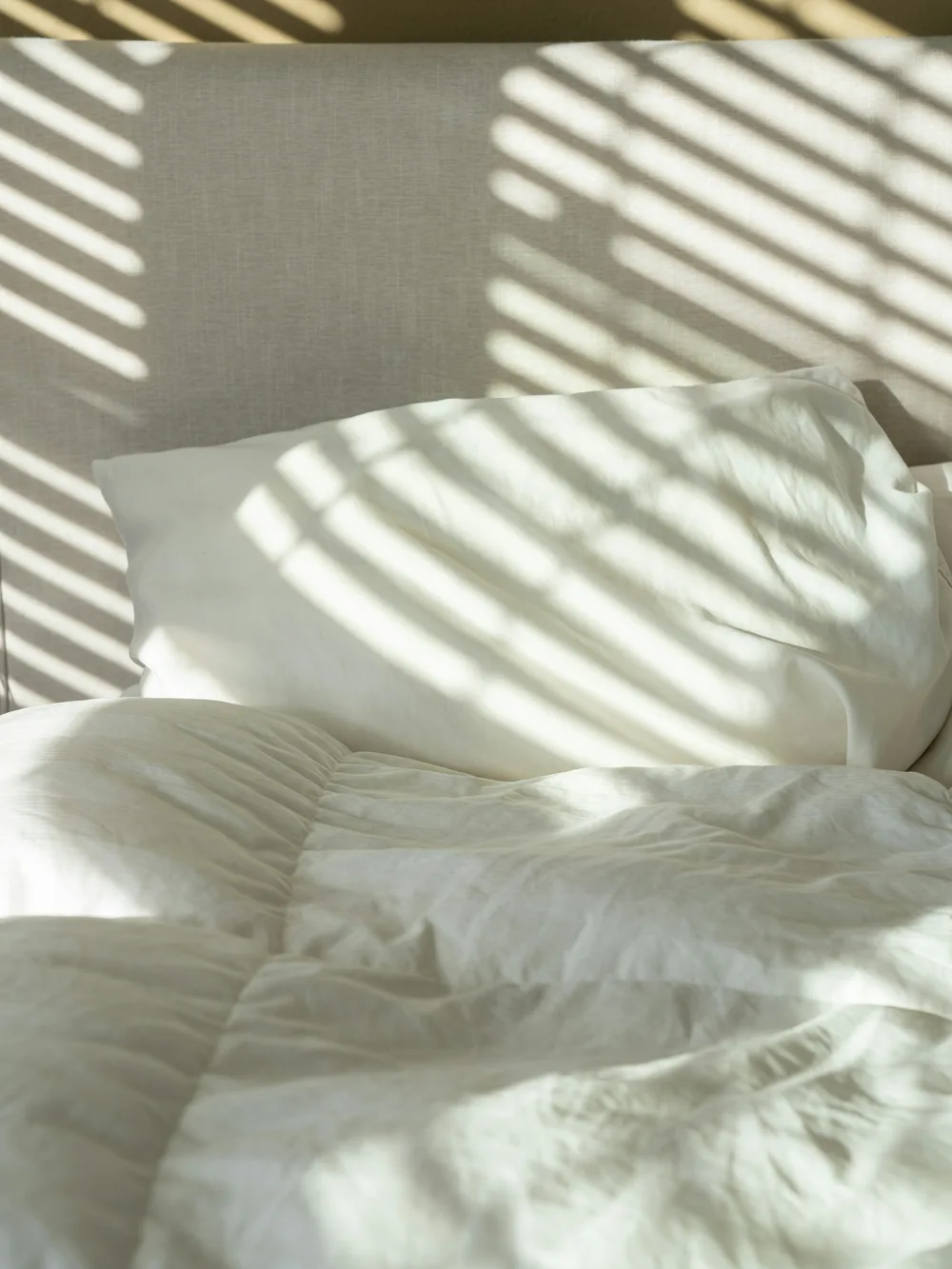 White linen bed with slatted sunlight across it