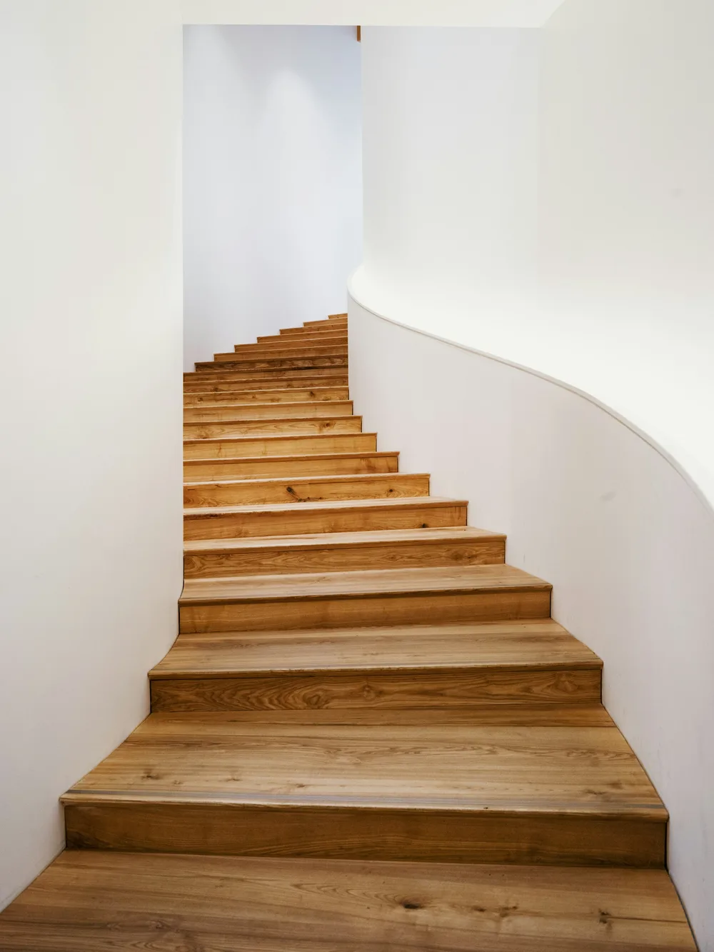 Curved oiled-oak stair against a white plaster wall