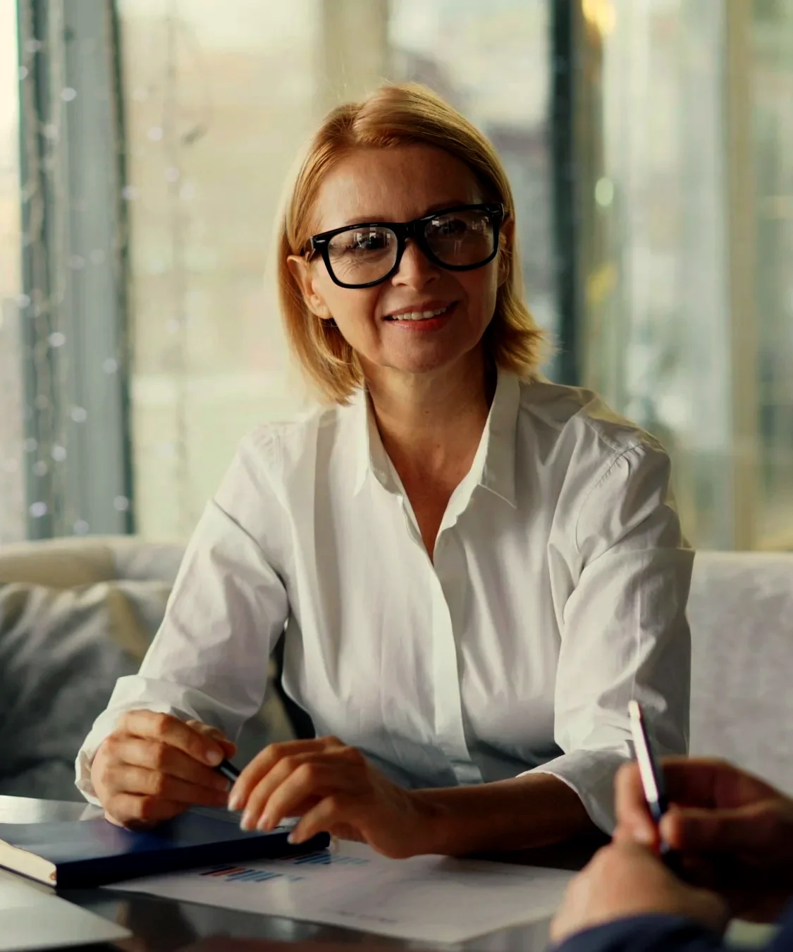 Ruth Marrow, in glasses and a white shirt, smiling across her desk at a client who is signing a form