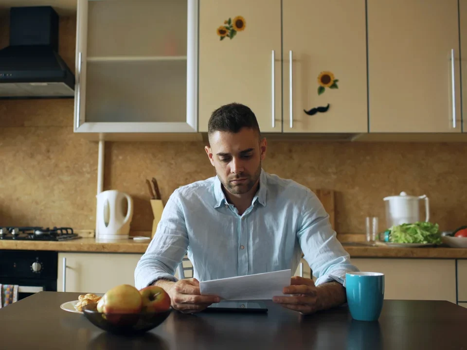 A man reading a letter from HMRC at his kitchen table with a mug of coffee