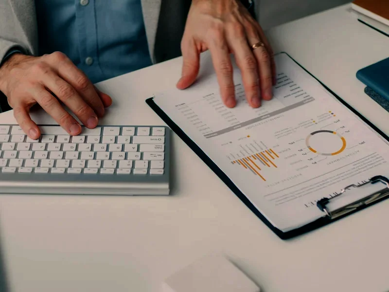 Hands sorting a client's statements and a clipboard of figures on a desk