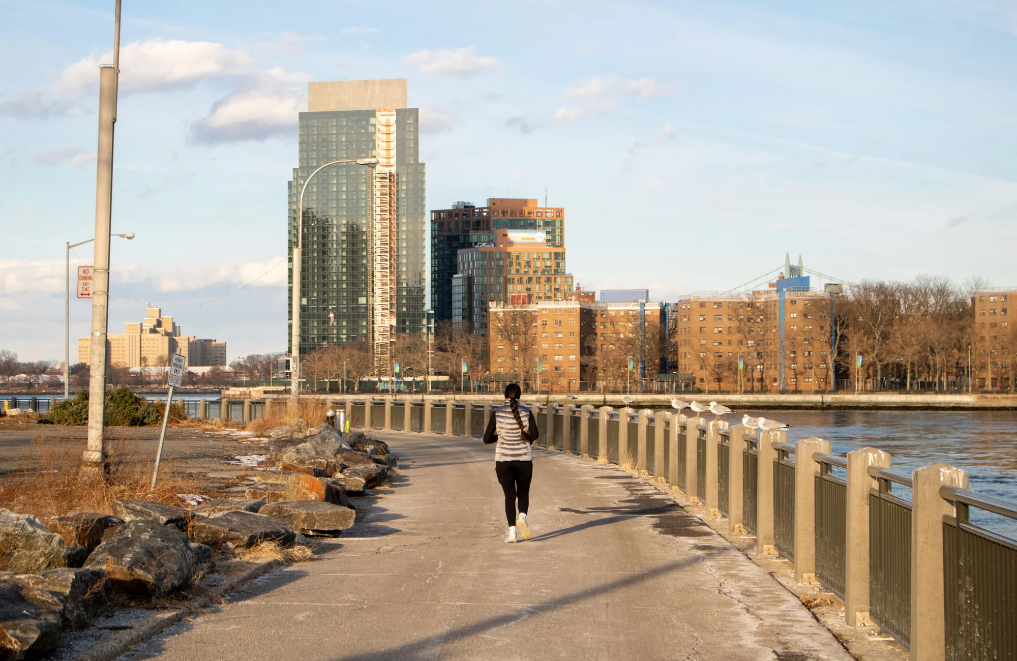 A runner heading along a riverside path in low afternoon sun