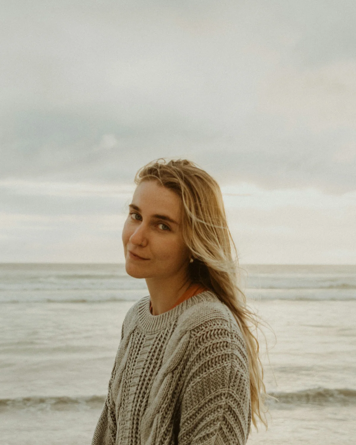 Freya, Saltmoor's founder, in a knitted jumper on the beach with the sea behind her