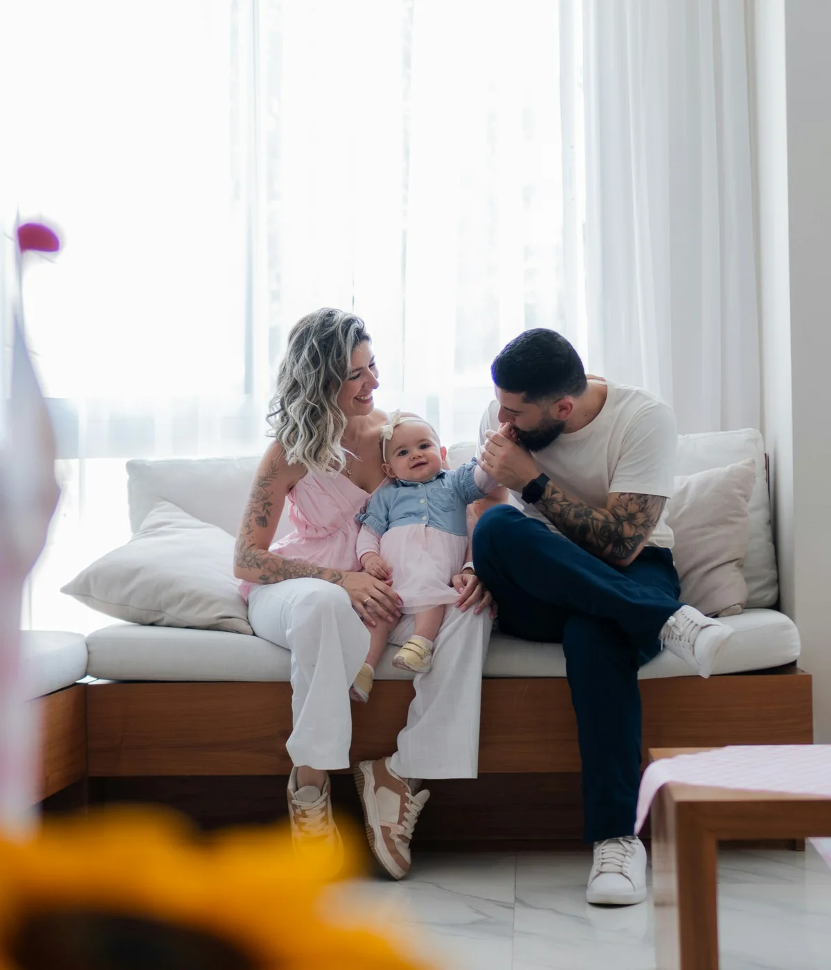 Parents relaxing with their baby on a white sofa in a sunlit living room