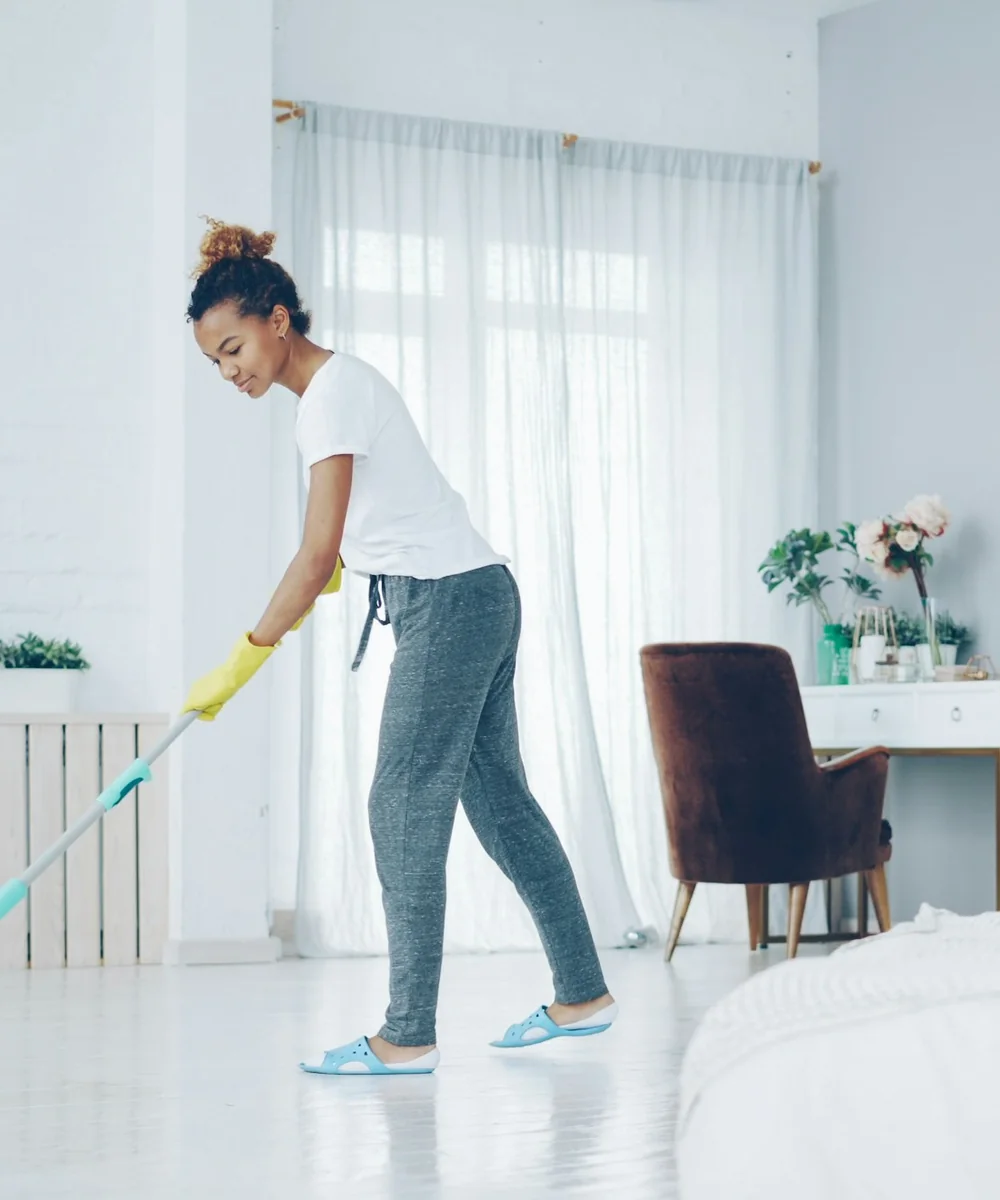 Cleaner mopping a bright bedroom floor beside white curtains