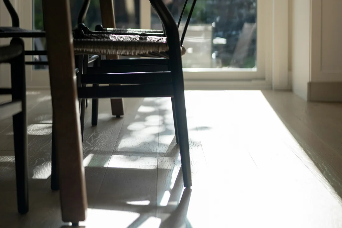 Late sun throws long chair shadows across a pale timber floor beside the dining table