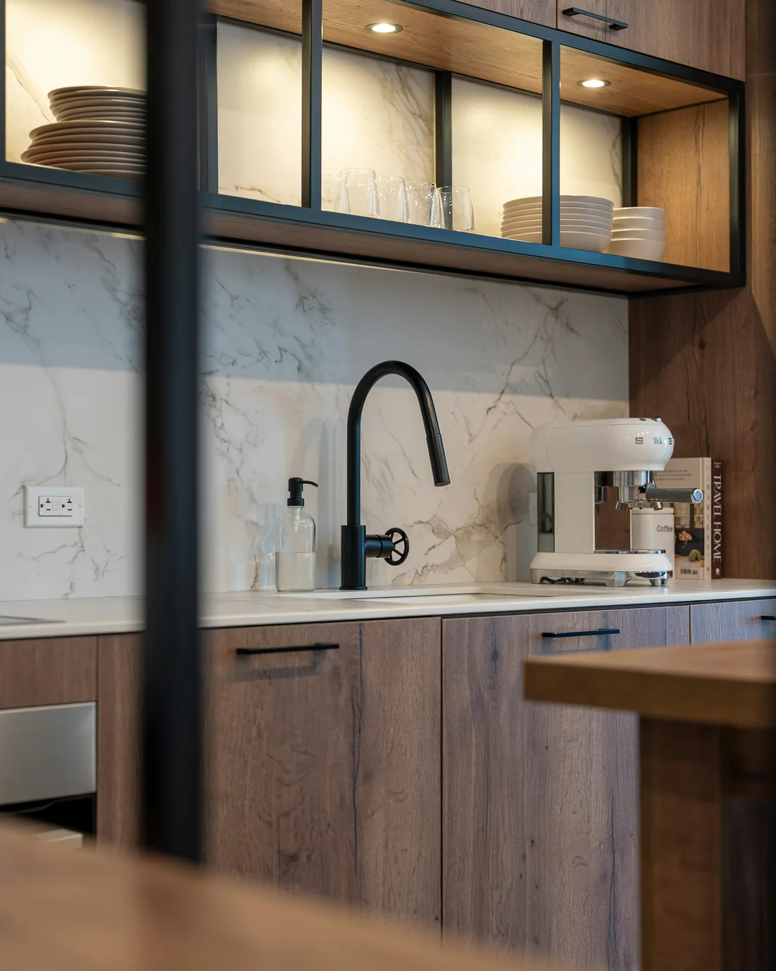 Timber-veneer cabinets, a marble splashback and a black tap under lit open shelves