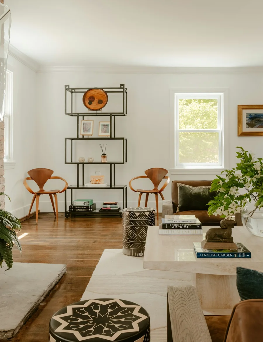 A bright living room with a brick fireplace, two timber armchairs and a pale sofa