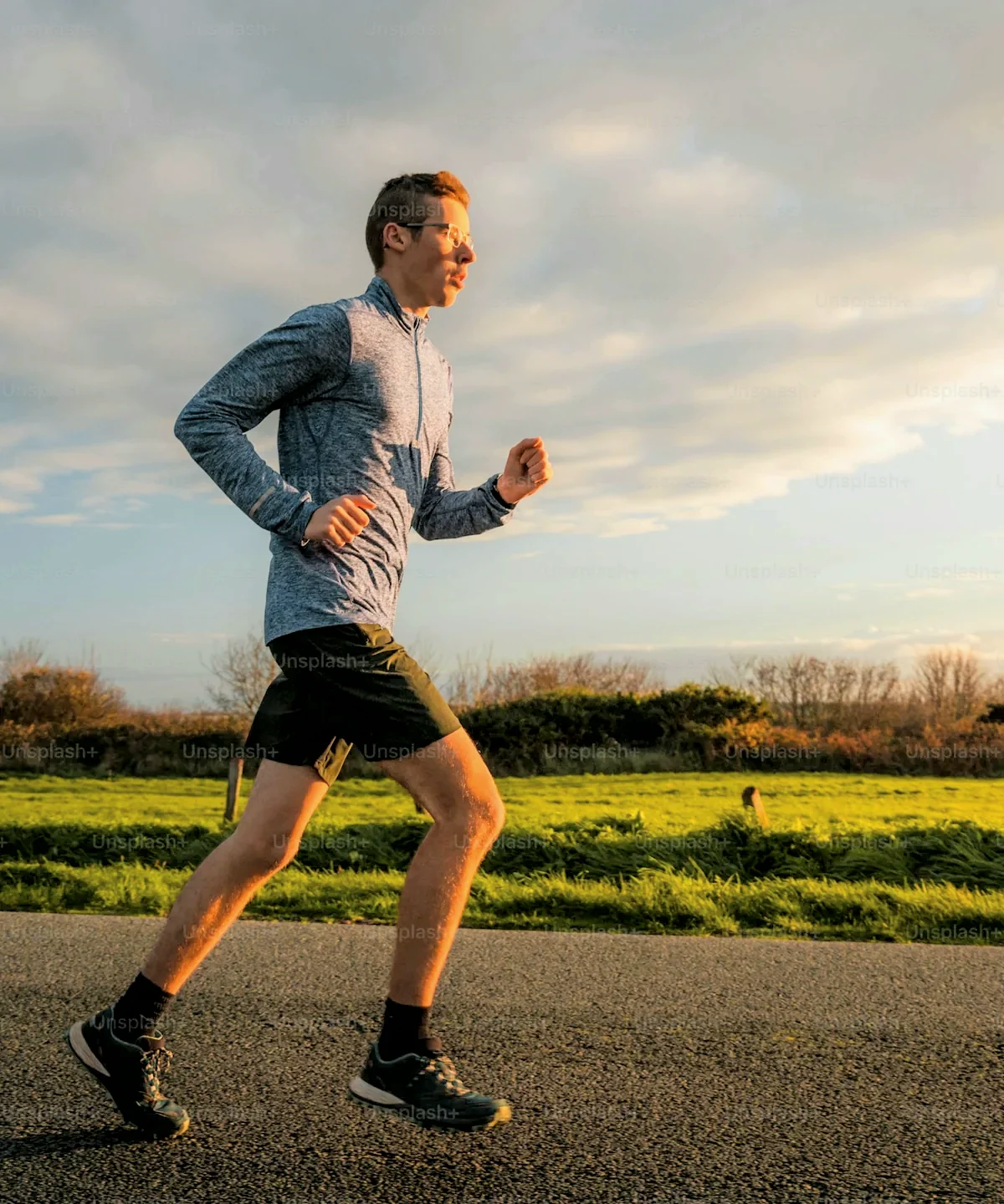 A runner mid-stride on a coastal road in golden evening light