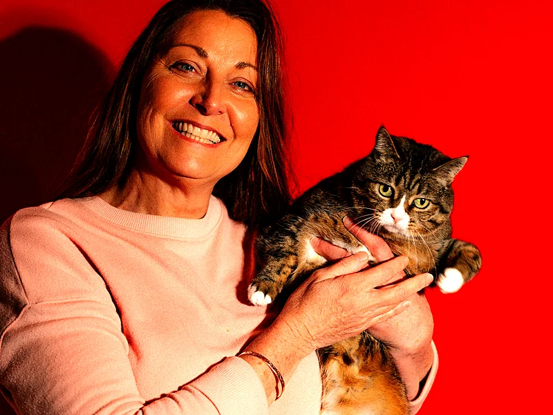 A smiling woman holding her tabby cat against a bright red wall
