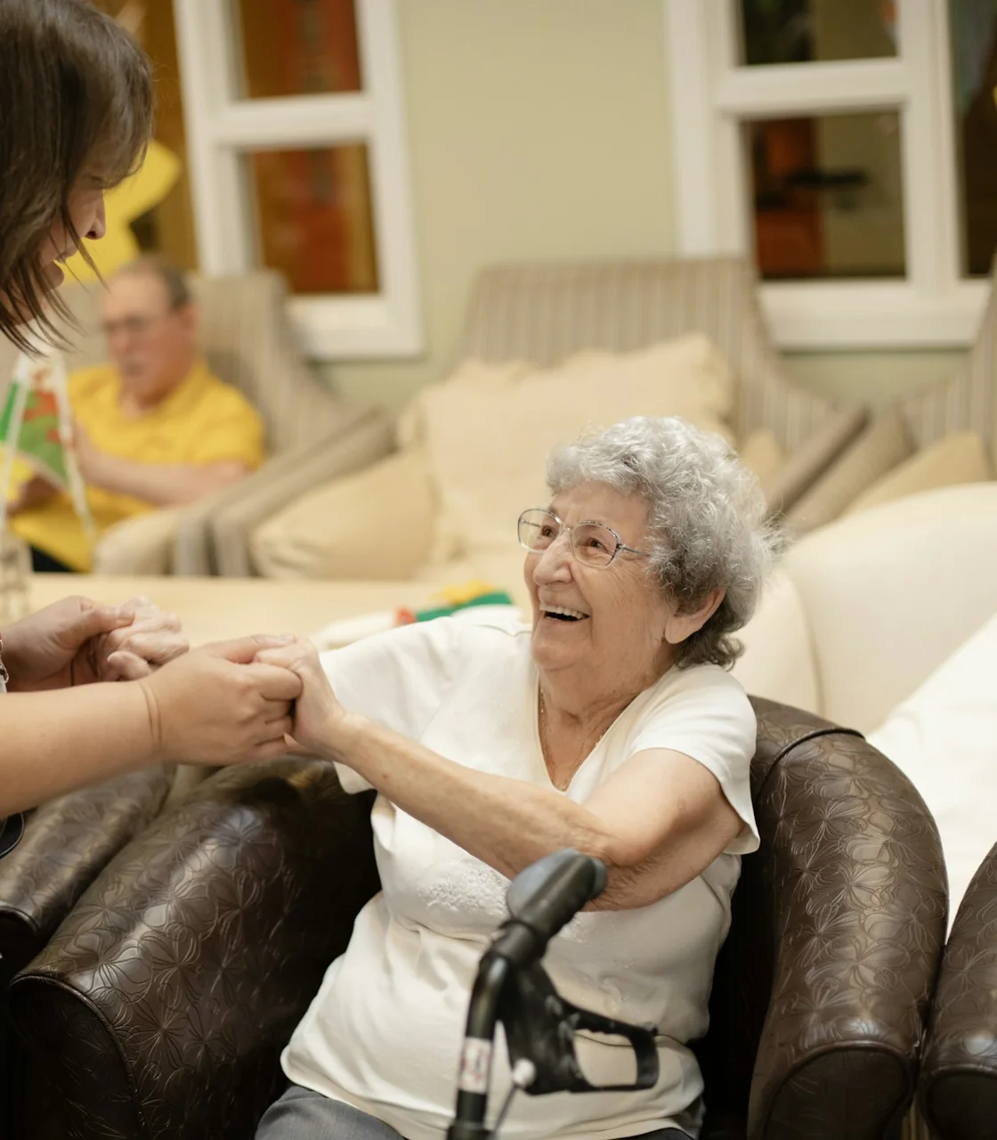 Resident laughing as her carer holds her hands in a care home lounge